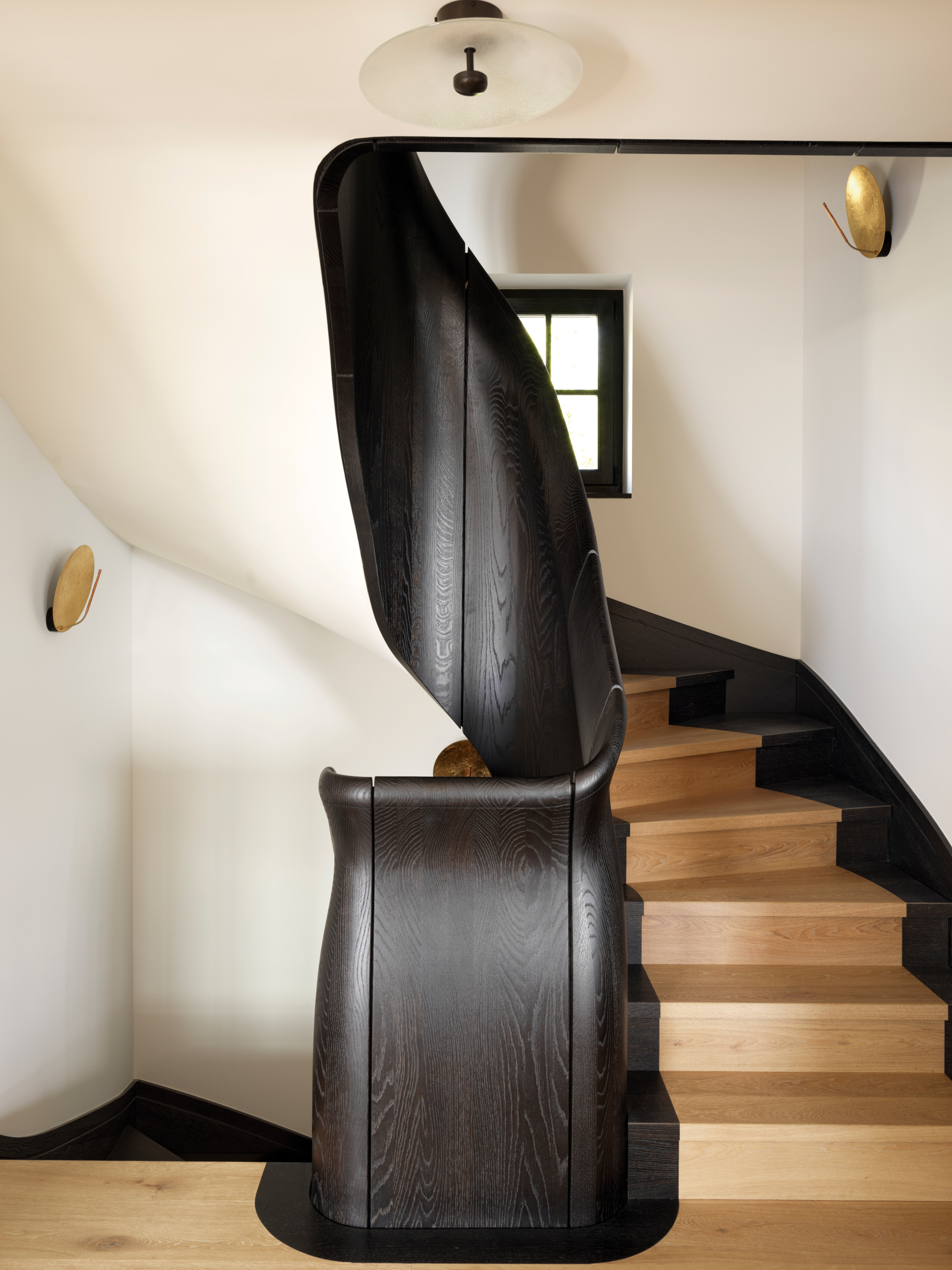 Curved staircase with black stained bannister and natural wood steps, with cream walls above