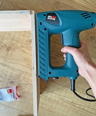 hand holding a nail gun up to a piece of wood