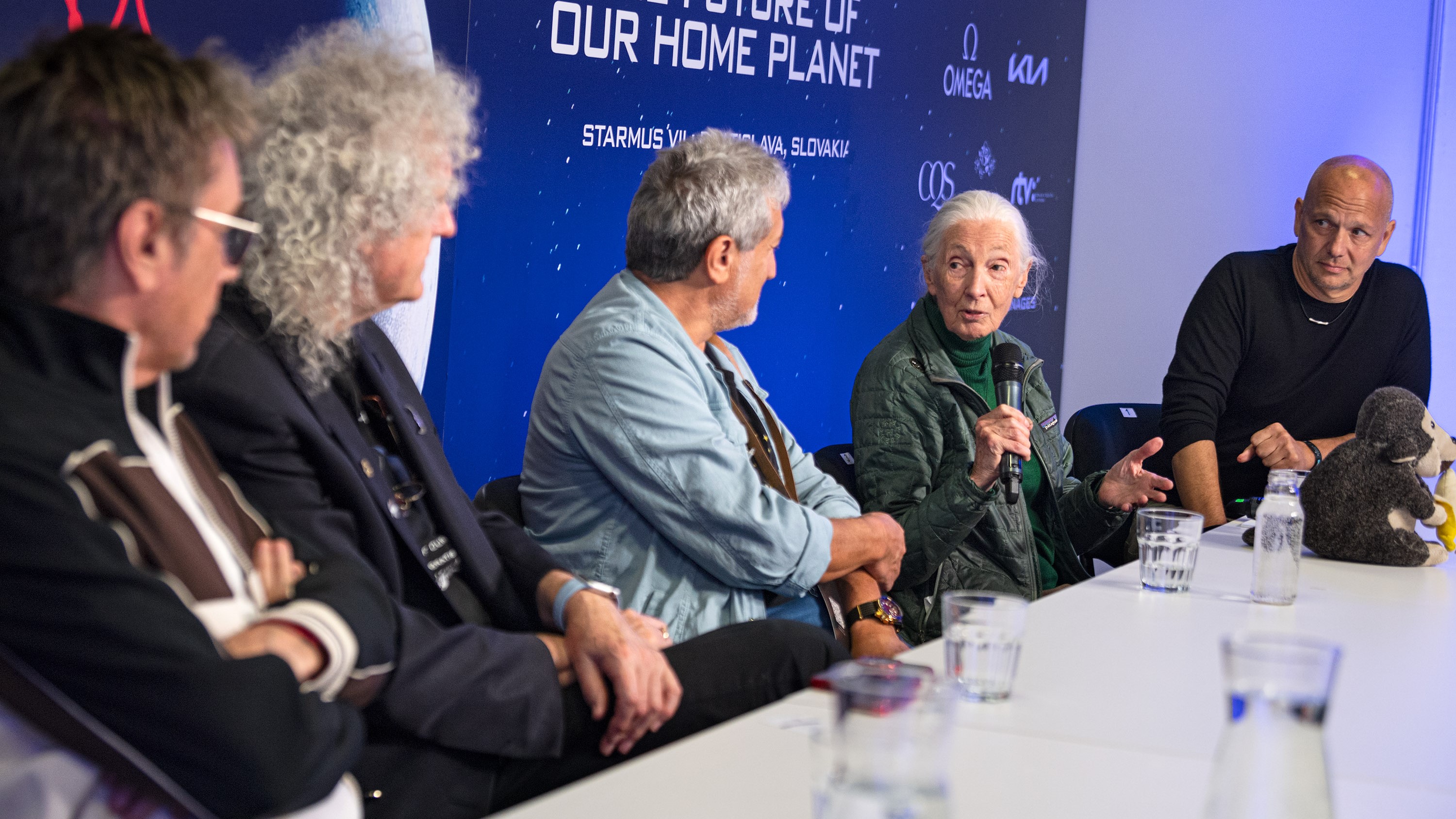 Opening press conference at Starmus festival shows five people sitting along a table and all looking at Jane Goodall who holds a microphone.