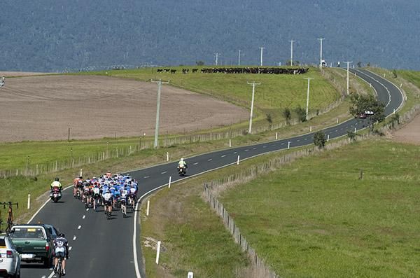 The peloton make their way towards the mountains and some interested spectators on the hill.