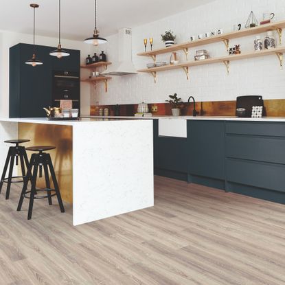 To illustrate can you paint laminate flooring – harrow grey oak laminate flooring in a modern kitchen with white island, dark bar stools, dark blue cabinets, gold splashbacks and white walls