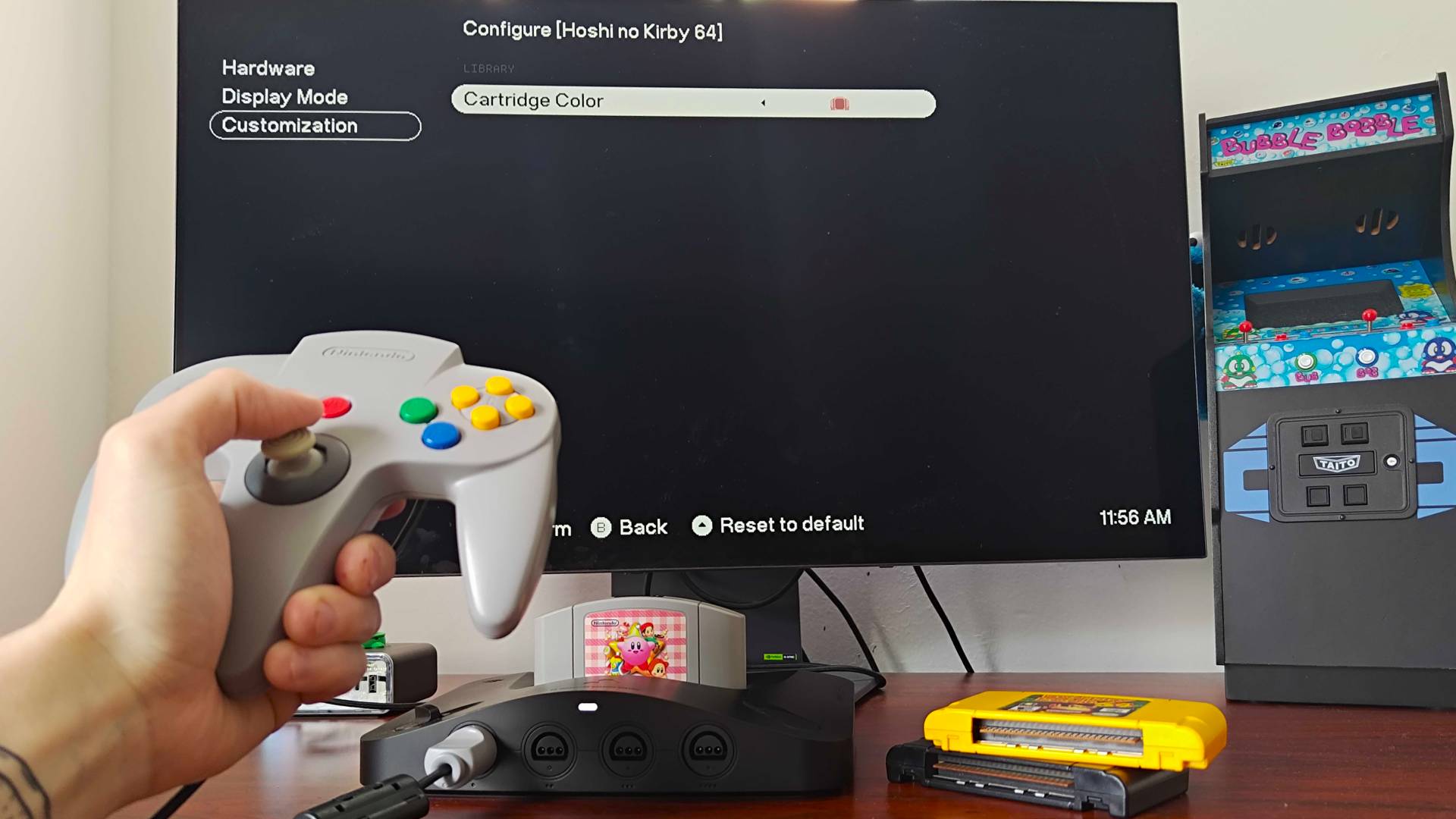 Hand using original N64 controller to select pink cartridge color in Analogue 3D settings menu for Kirby 64.