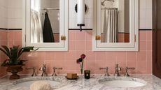 bathroom with a marble topped double vanity with nickel hardware and a pair of mirrored bathroom wall cabinets with pink square wall tiles and a black border between white tiles above
