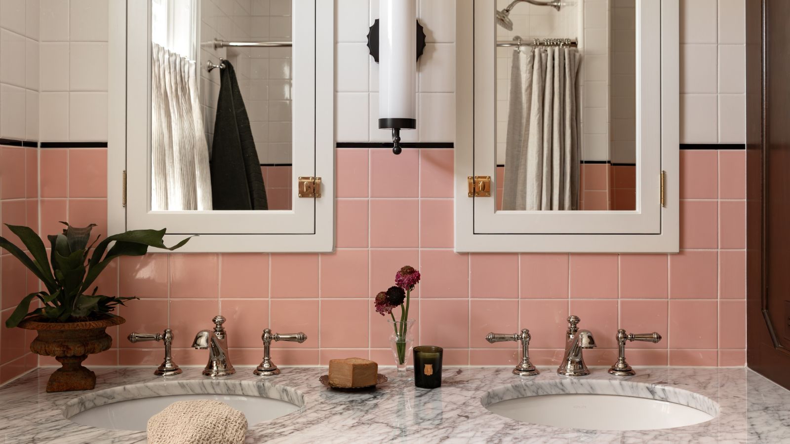 bathroom with a marble topped double vanity with nickel hardware and a pair of mirrored bathroom wall cabinets with pink square wall tiles and a black border between white tiles above