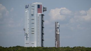 a brown and white rocket rolls vertically toward a large white building, with cloudy blue skies in the background