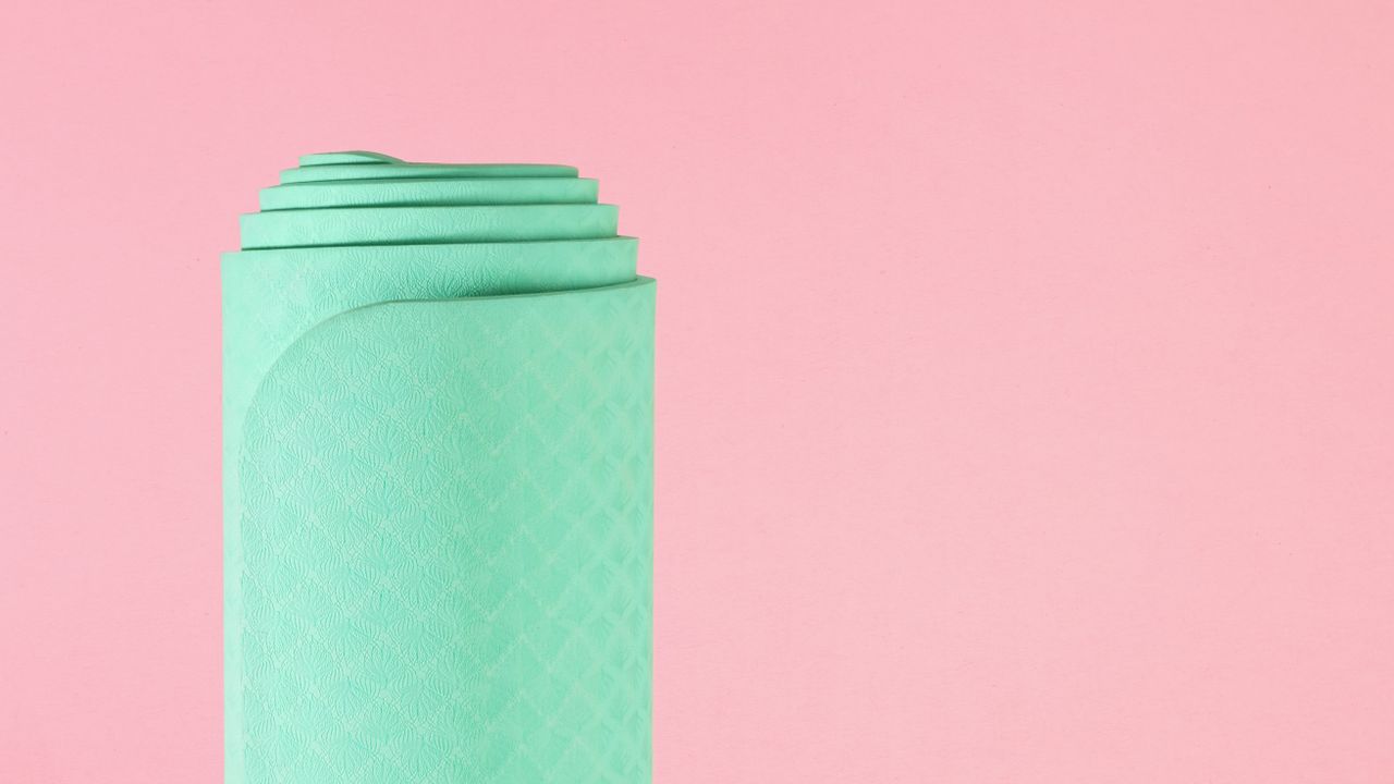 rolled up green yoga mat on pink background 