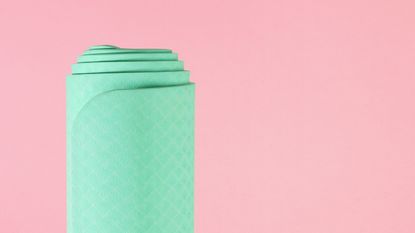 rolled up green yoga mat on pink background 