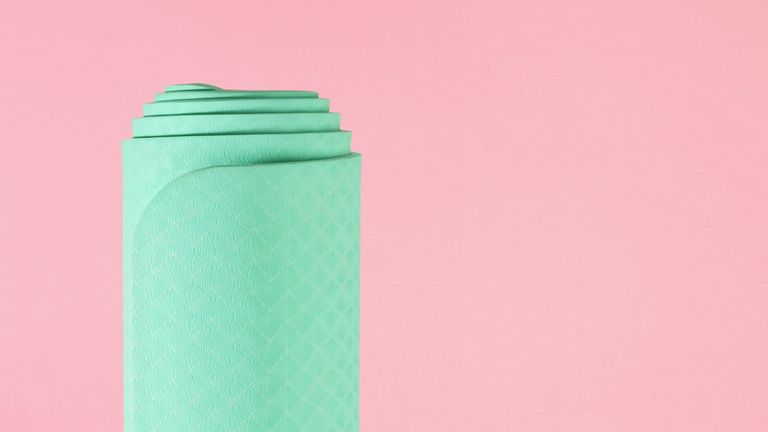rolled up green yoga mat on pink background