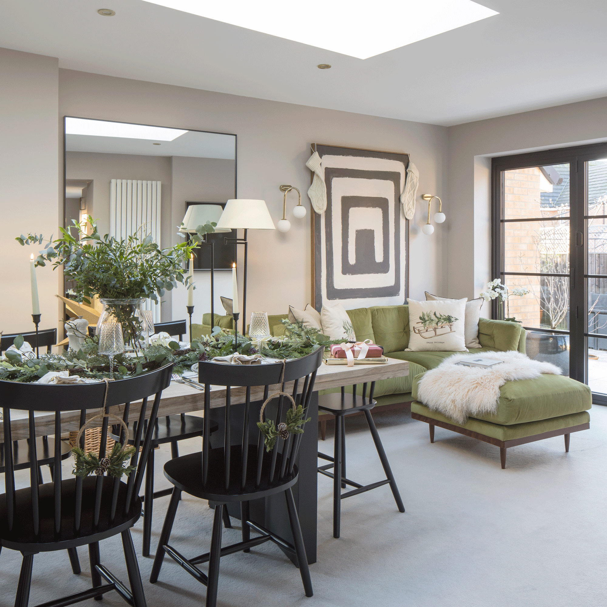 a large open plan dining living area with a dining table with black chairs set for Christmas and a green chaise sofa