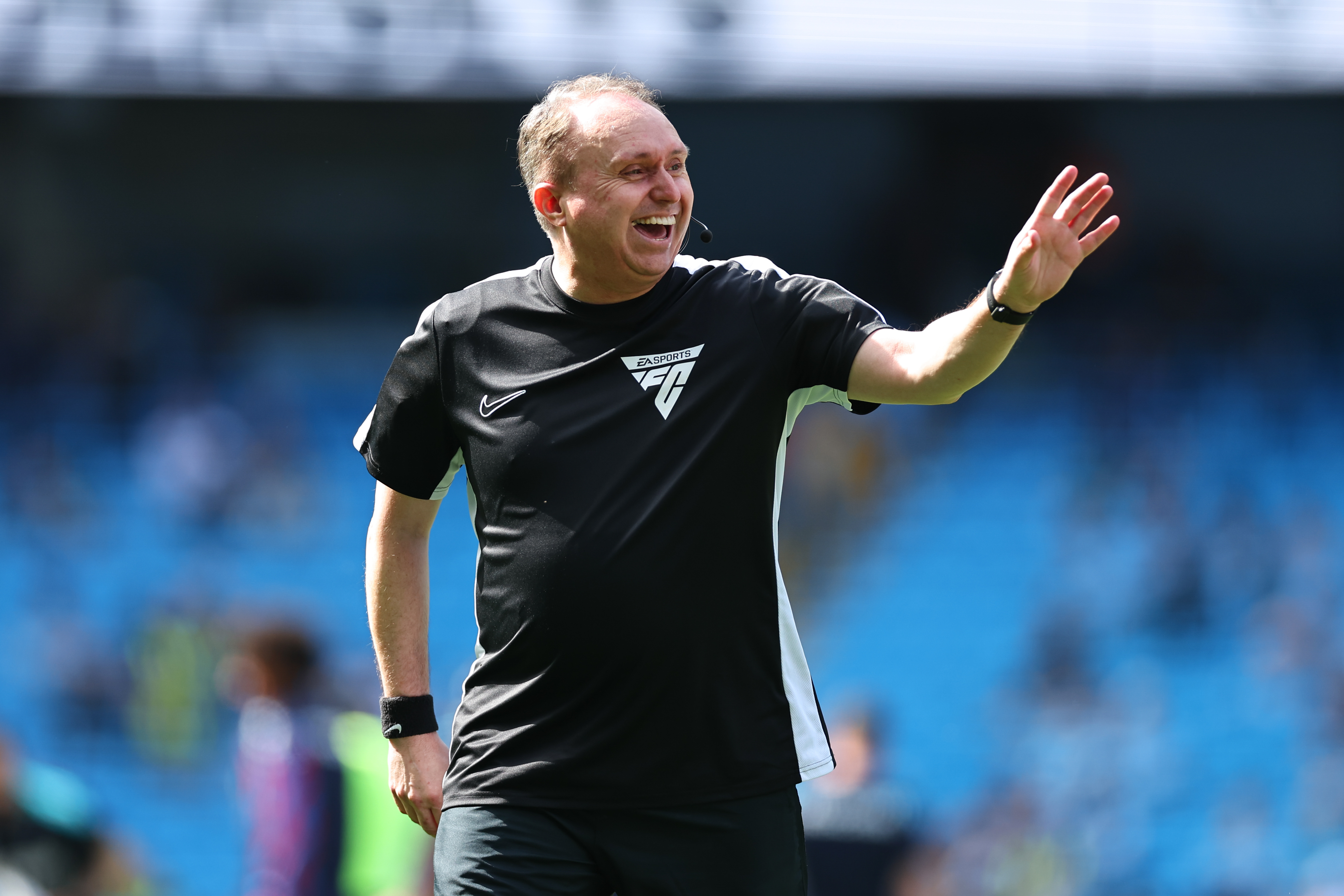 Assistant referee Darren Cann smiling and waving on a football pitch before a match.