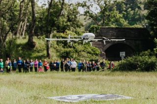 Skyports drone landing in a field on a mat with onlookers in the background