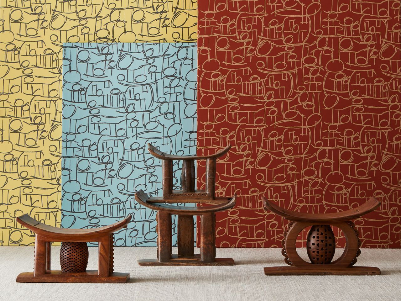 The &#039;Sella&#039; textile covers the wall in yellow, blue and red, with line and circle patterns on it. In from of the wall are the traditional Ghanaian asesegua seats made out of wood.