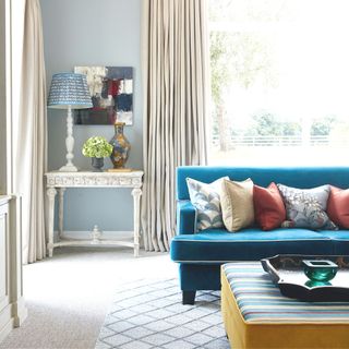 living room with blue walls cream floor length curtains and a bright blue velvet sofa