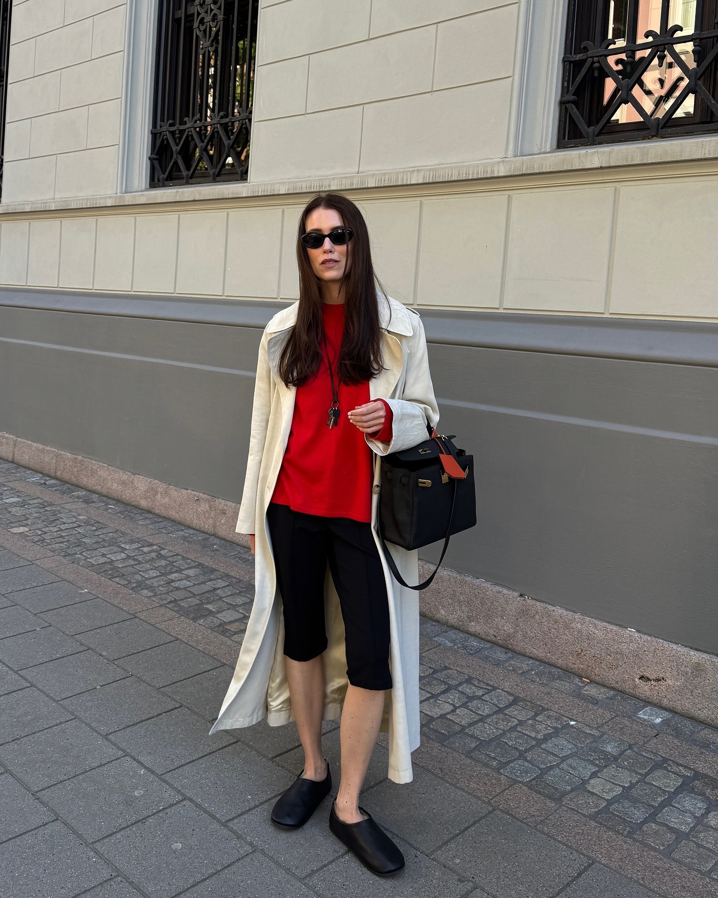 @annabelrosendahl wearing a cream trench coat, red T-shirt, and black capri pants.