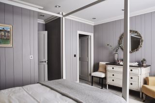 Bedroom with four poster bed, grey panelled walls, white painted chest of drawers, and upholstered chairs