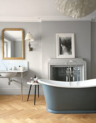 Light grey bathroom idea with dark freestanding bath, marble sink and gold mirror