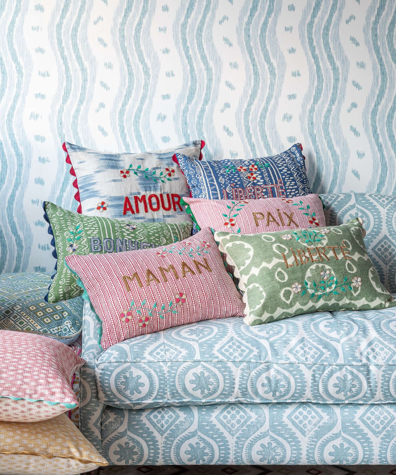 Wicklewood decorative pillows with embroidered edges and scalloped on a blue sofa with blue wallpaper