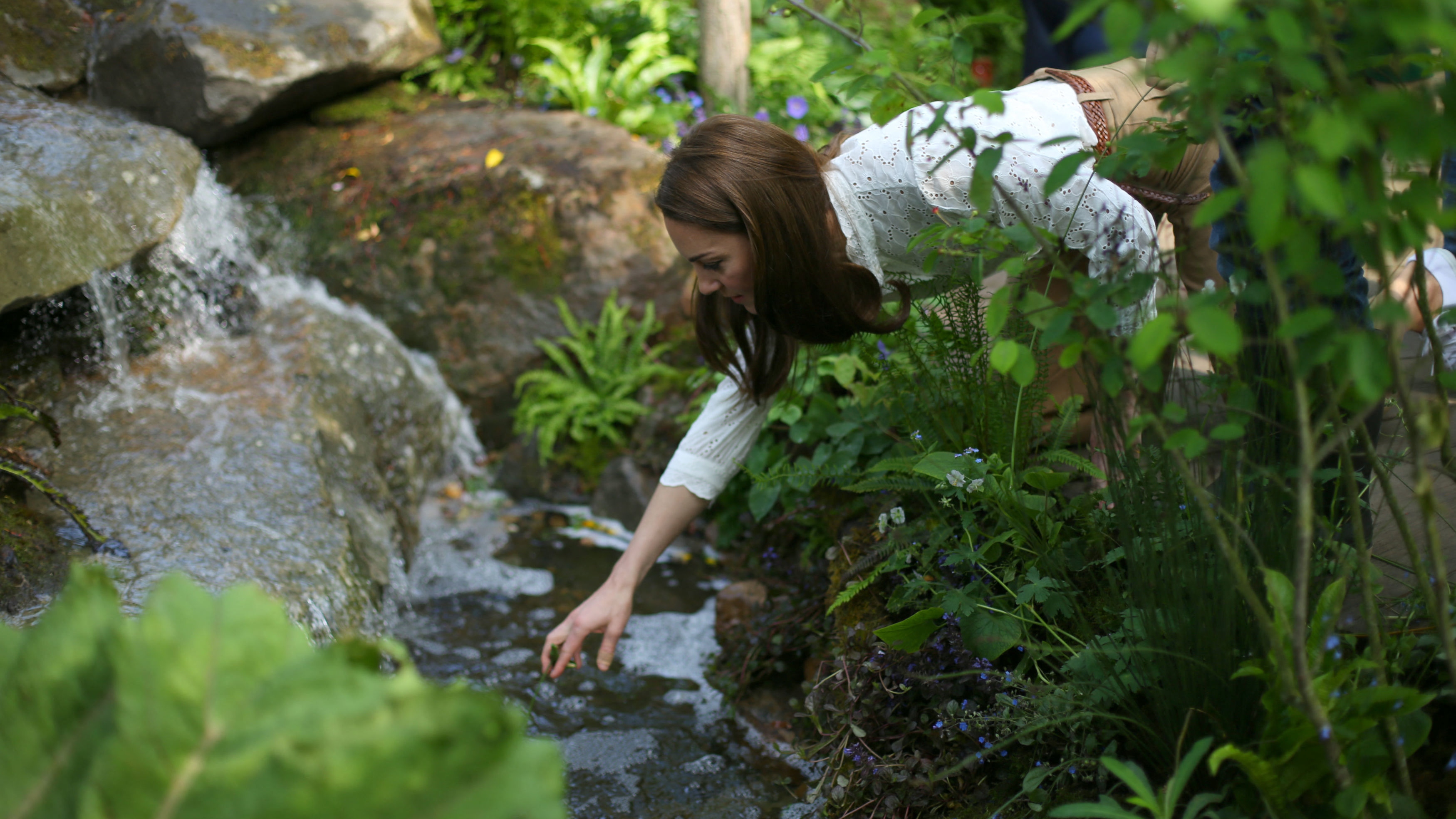 Catherine, Princess of Wales reaches into a pond as she visits the 'Back to Nature Garden' garden, that she designed at the 2019 RHS Chelsea Flower Show