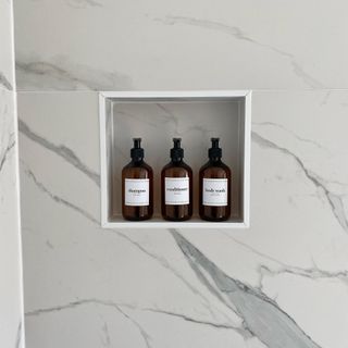 shower wall with marble tiles and alcove with toiletries