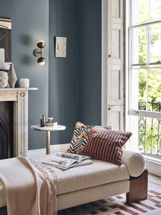 A boucle chaise longue next to the window with a wall backdrop painted a smoky blue