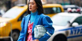 Woman in a blue coat clutches a pale blue handbag under her arm.