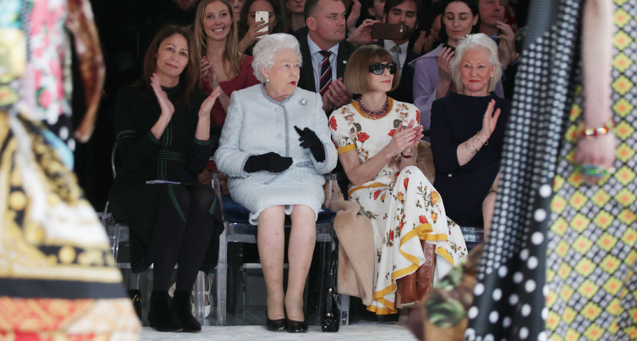 Queen Elizabeth sitting at a fashion show with Anna Wintour and Angela Kelly