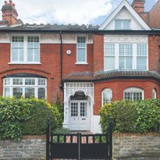 Exterior of a red brick period house with a grey front door and patterned pathway behind a grey front gate