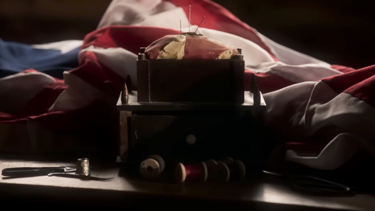 A screenshot from The American Revolution of a flag being sewn