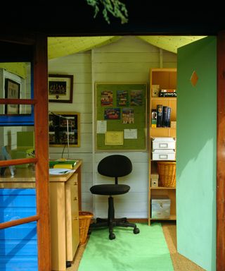 Doors open to garden shed converted into office with green rug and black office chair