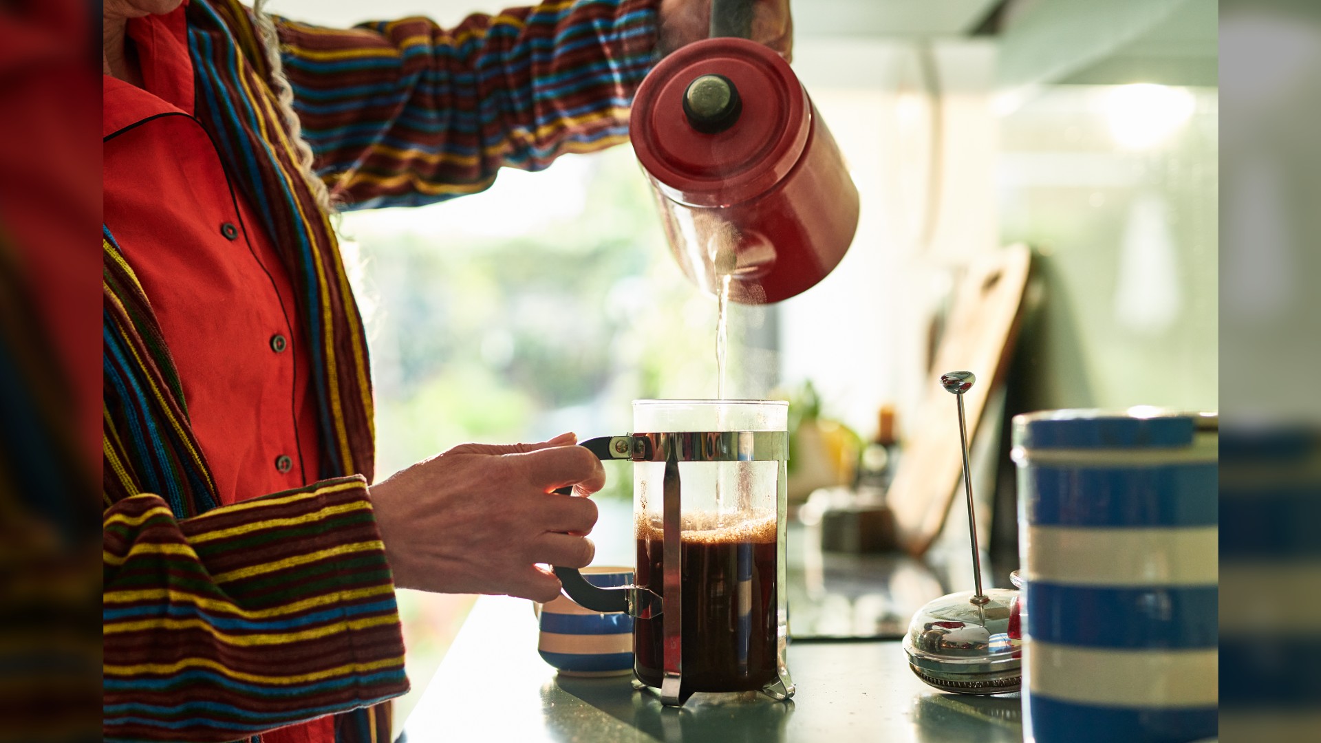 Close up of senior woman wearing pyjamas and a bath robe pouring boiling water into a cafetiere.