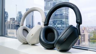 Hero image for best Sony headphones showing Sony WH-1000XM5 in black and ecru (off-white) color versions against a office window