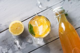 Glass bottle of kombucha lemonade with lemon sitting on wooden table with glass of kombucha and lemon