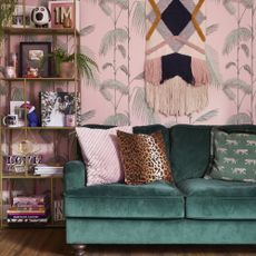 Living room with pink tropical wallpaper and green velvet sofa.
