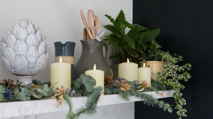 Wooden shelf with candles and glass vases holding moss, pine cones and eucalyptus