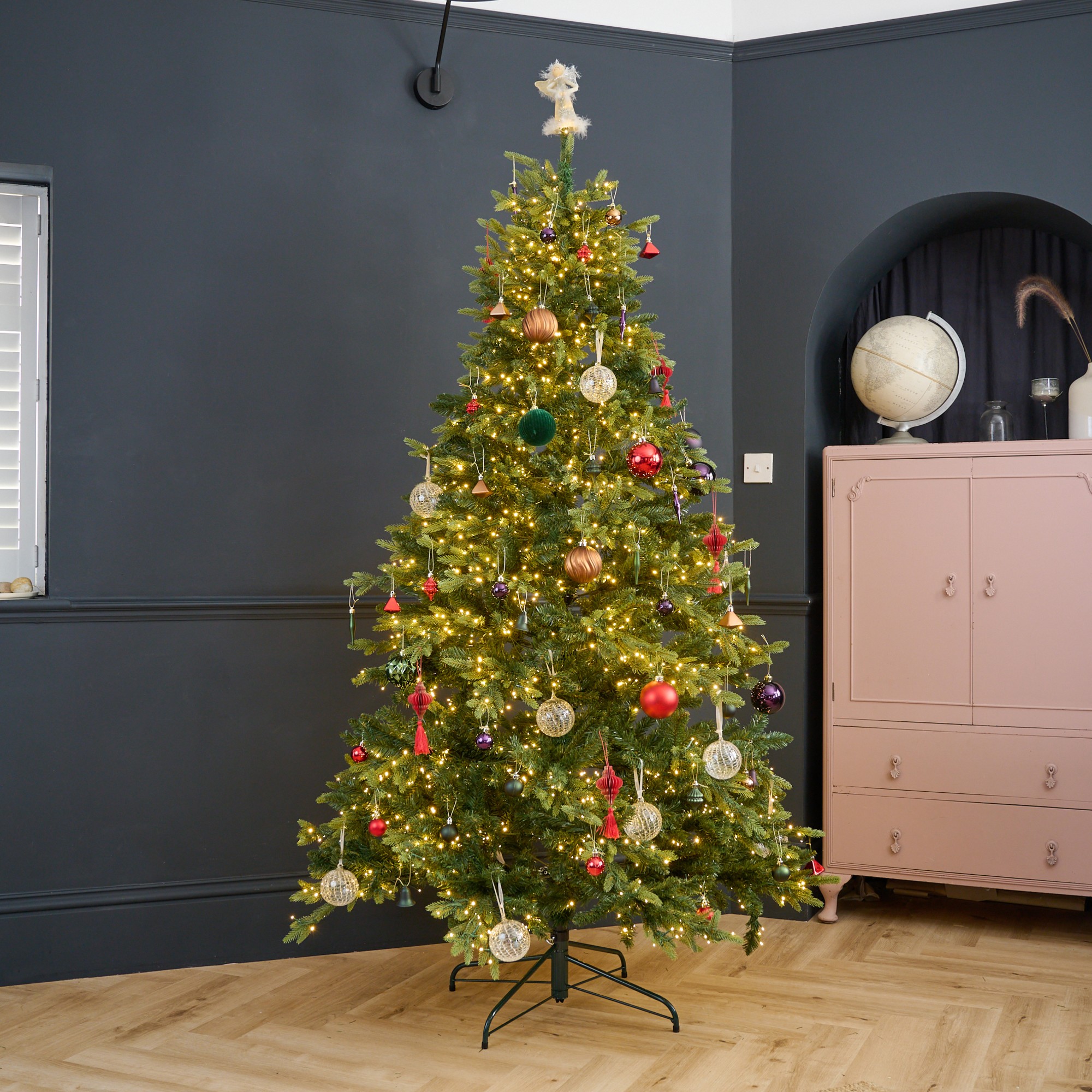 Habitat's 7ft Pre Lit Natural Look Christmas Tree decorated with Christmas baubles in a black-painted living room