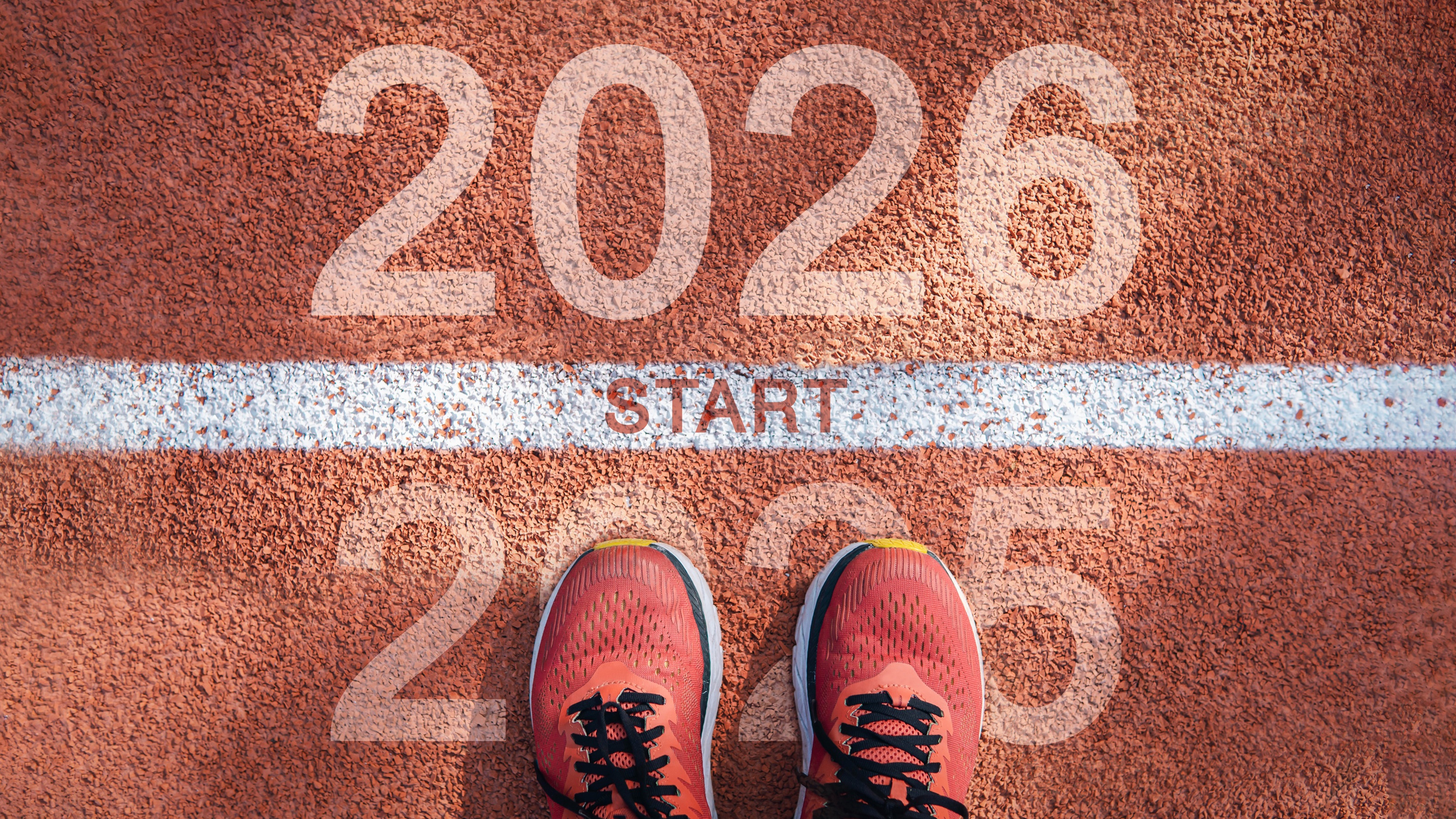 A pair of sneakers resting on the year 2025 at a startling line with 2026 on the opposite side.