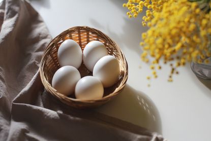 five white eggs in a tan basket set beside yellow flowers