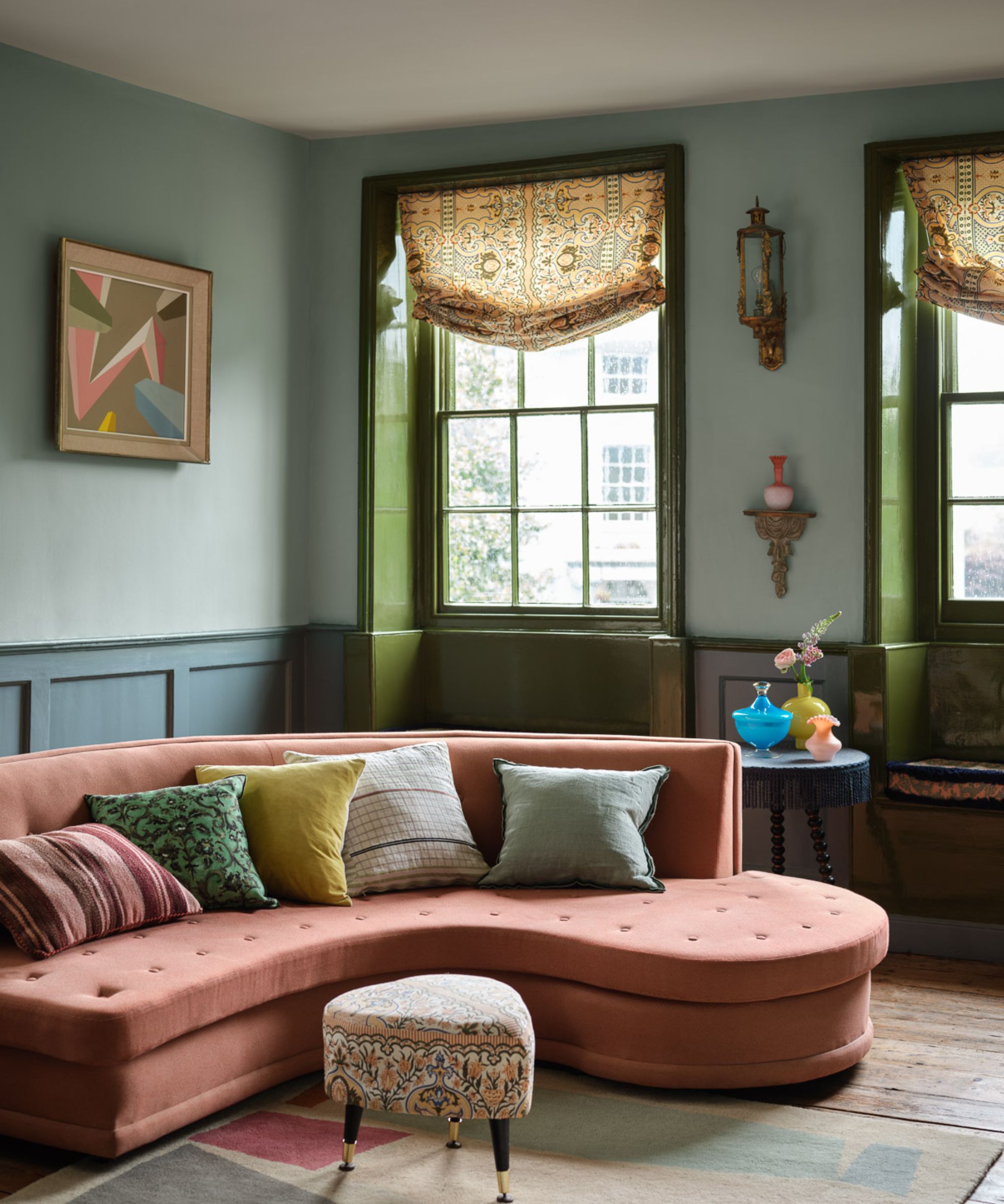 living room with blue-green two-tone walls, a muted pink chaise sofa, and two windows with green gloss woodwork