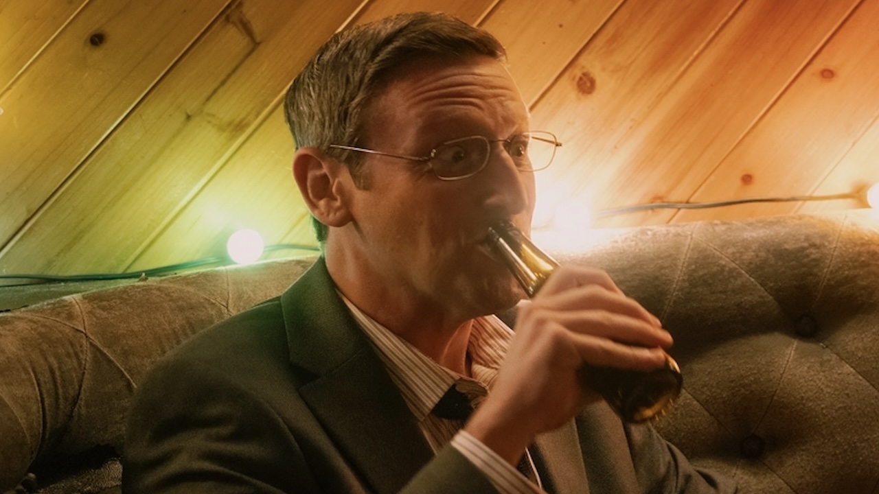 Ron drinking from.a beer bottle in club in The Chair Company Episode 4