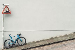 A blue bike against a grey wall with a 16% gradient sign