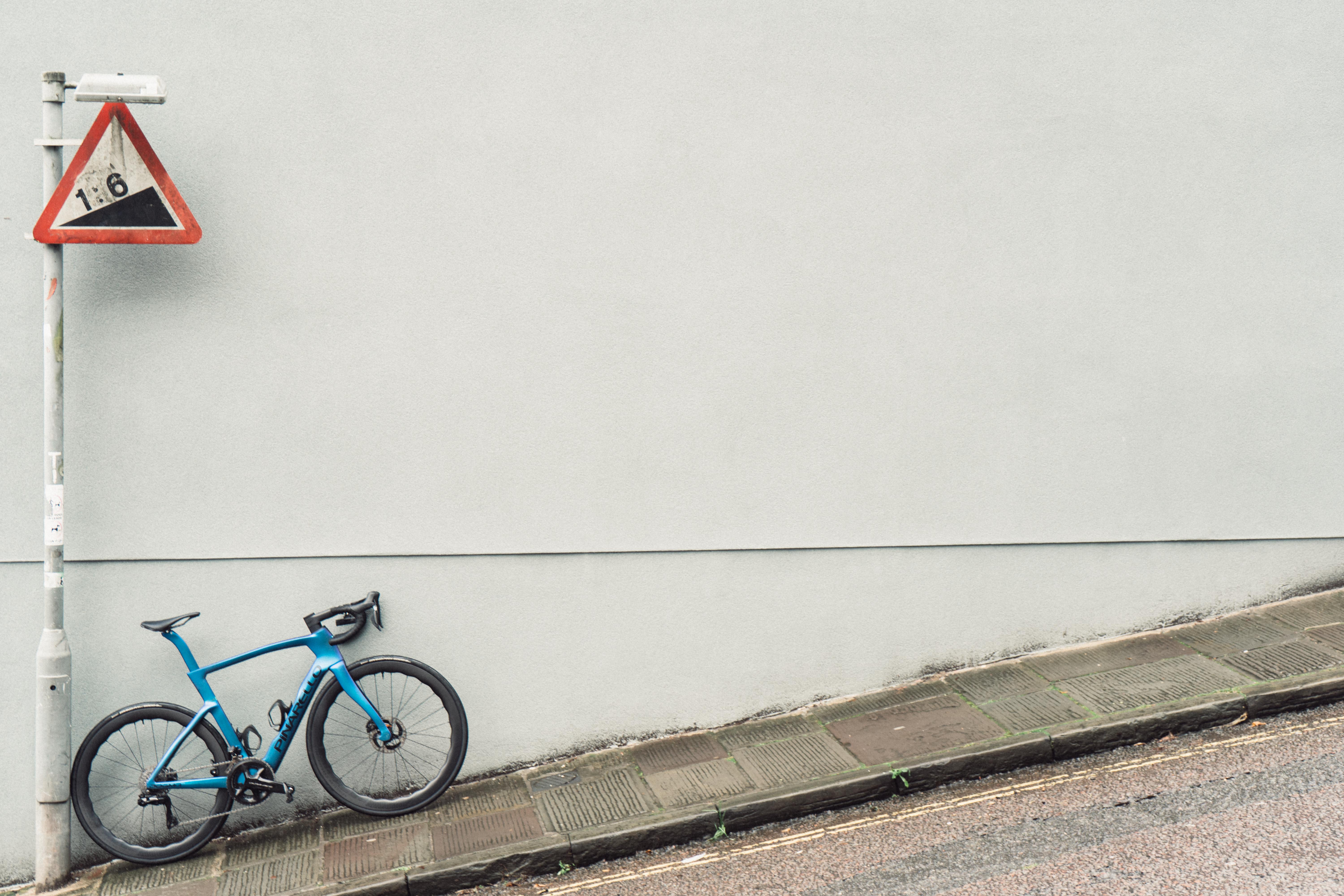 A blue bike against a grey wall with a 16% gradient sign