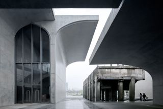 The Long Museum West Bund is a concrete structure. The part of the concrete roof continues over the edge, providing shelter from the weather. The entrance to the building is glass, and it goes up high with a curved top.