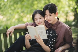 a woman reads a book and leans against a man with his arm propped on a bench