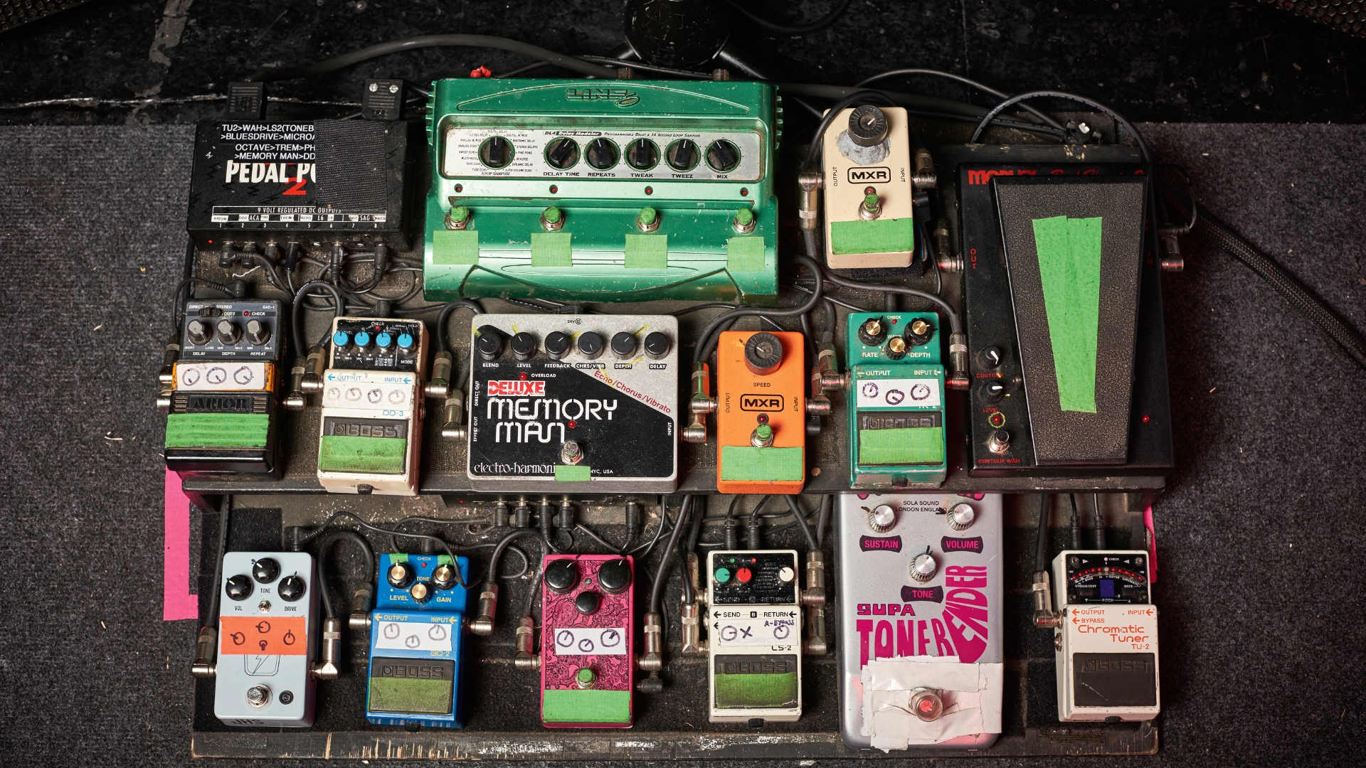 A large, two-tier pedalboard with various pedals lying on a floor