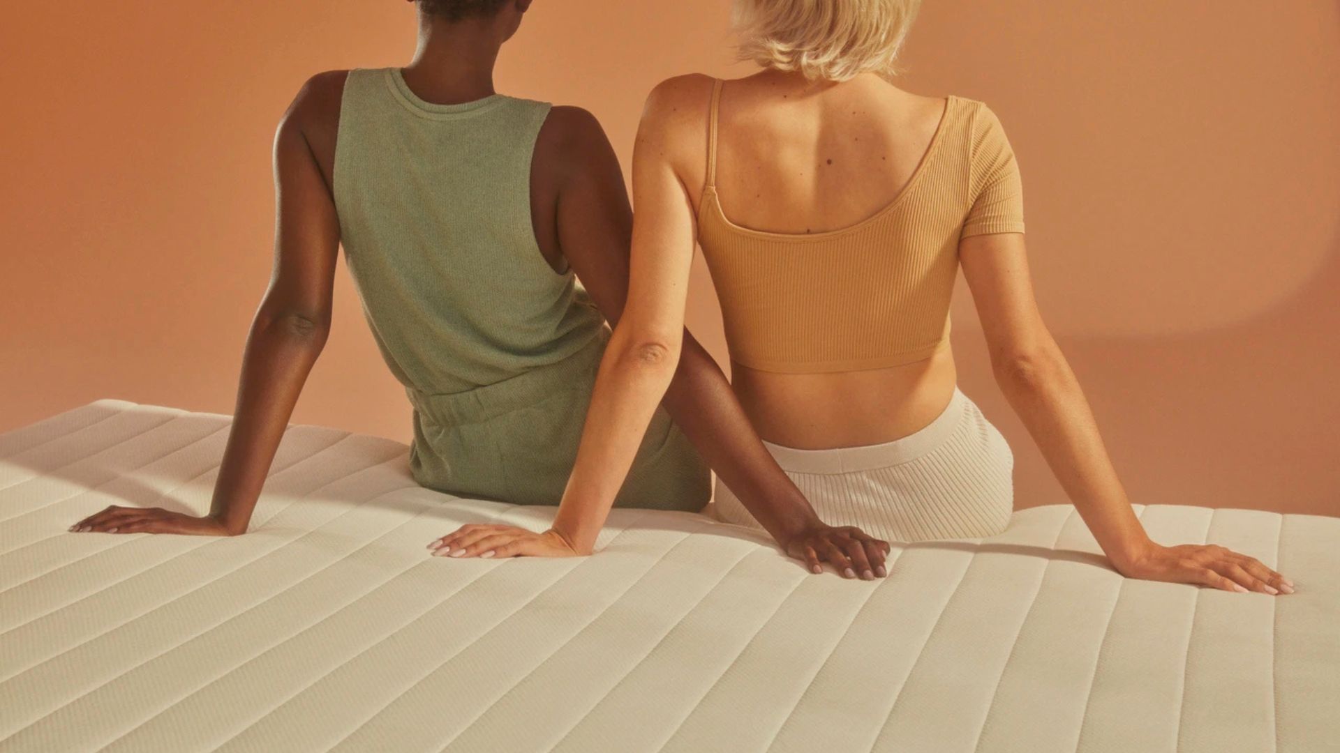 Two women sat with their back to the camera on top of the GOTS certified Earthfoam mattress, leaning back with their arms crossing over each other