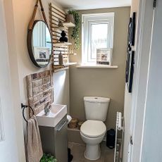 a scandi style cloakroom with grey vinyl flooring, matching vanity sink with a brick splashback, white toilet and a wooden shelf feature on the wall