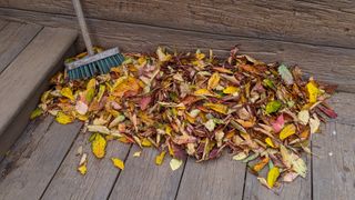 a broom next to a pile of leaves to show a step in how to clean decking