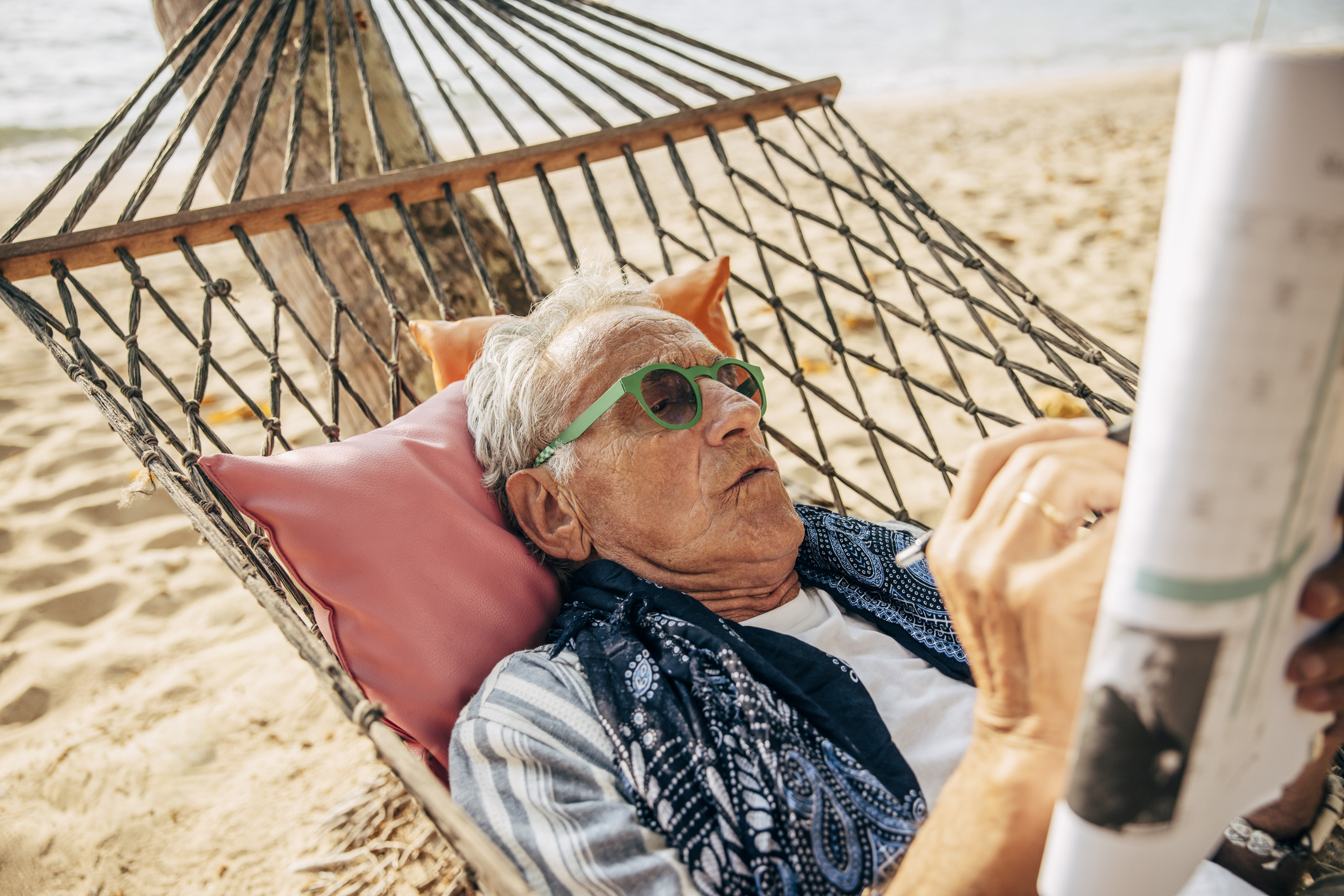 Senior man solving puzzle in newspaper while lying in hammock on beach