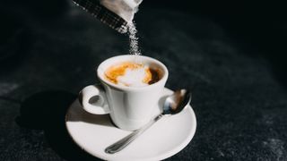 Sweetener being poured in espresso in china cup