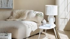 living room with light beige walls, sculptural white sofa, white side table and lamp, window with lots of natural light